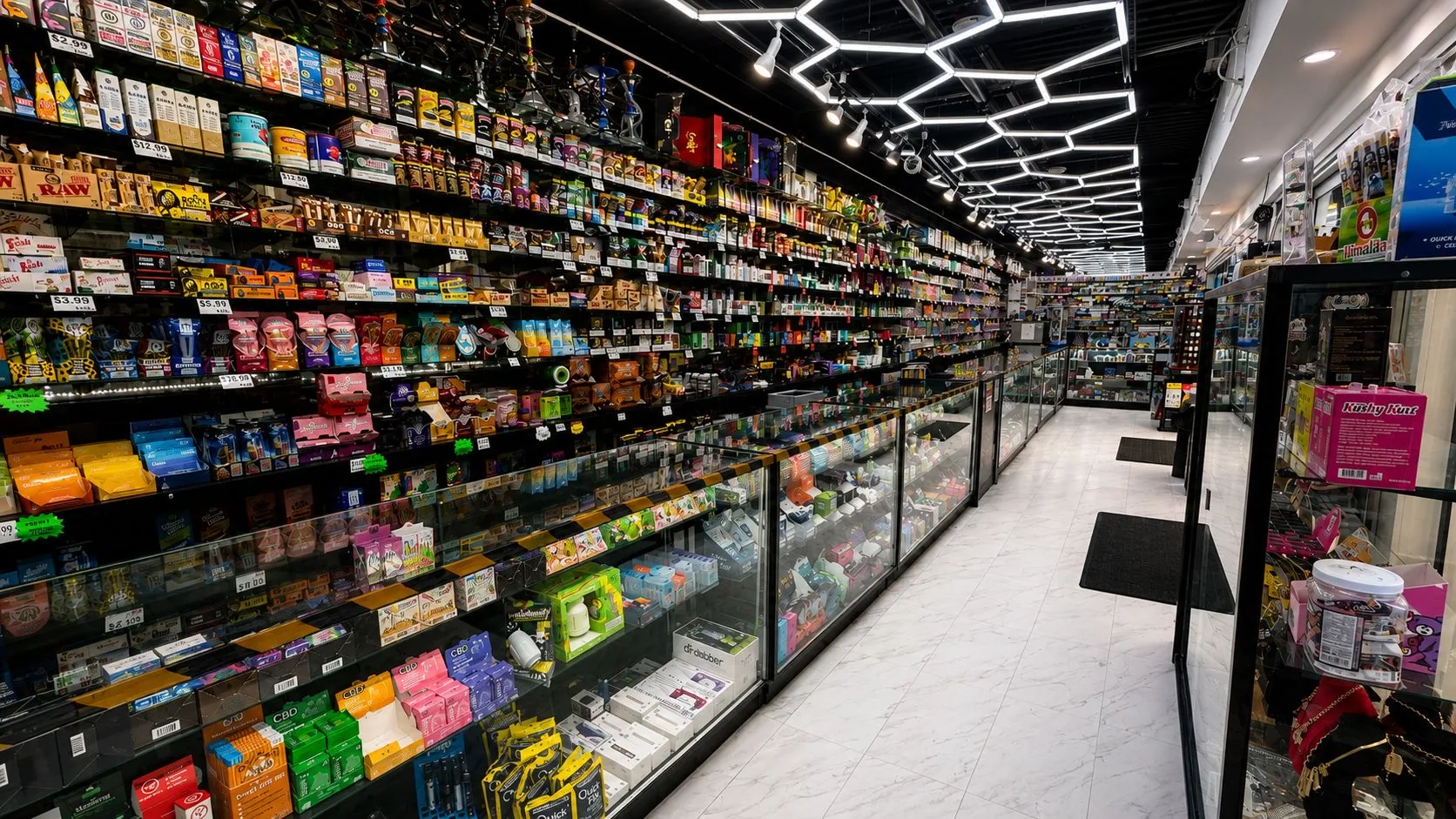Inside Puff Vegas: the aisle of glass cases and the wall of vapes, cigars and rolling papers under hexagon lights.