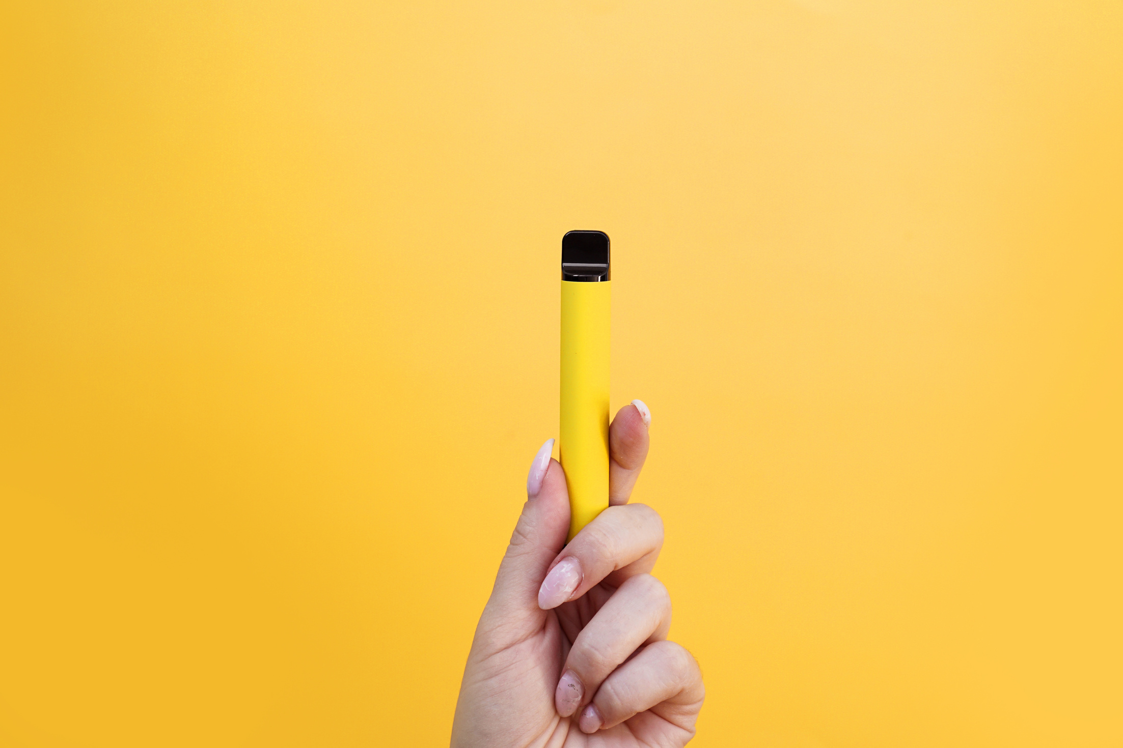 Yellow Disposable Electronic Cigarette in Female Hand. Bright Yellow Background